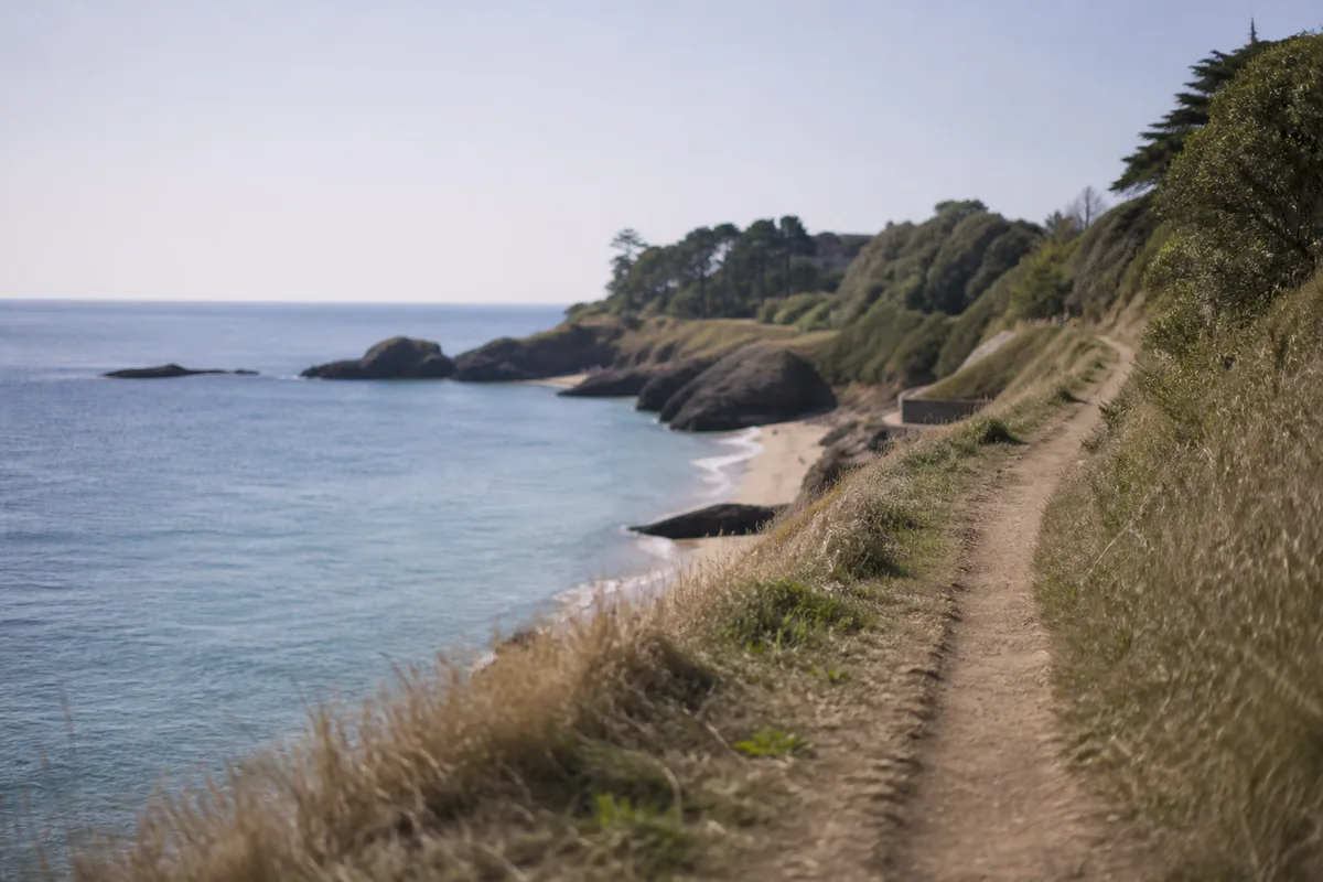 Sentier côtier étroit longeant des falaises basses et des criques de sable